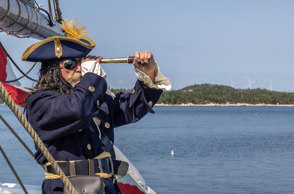 Pirate in blue outfit looking through spyglass on ship by the sea.